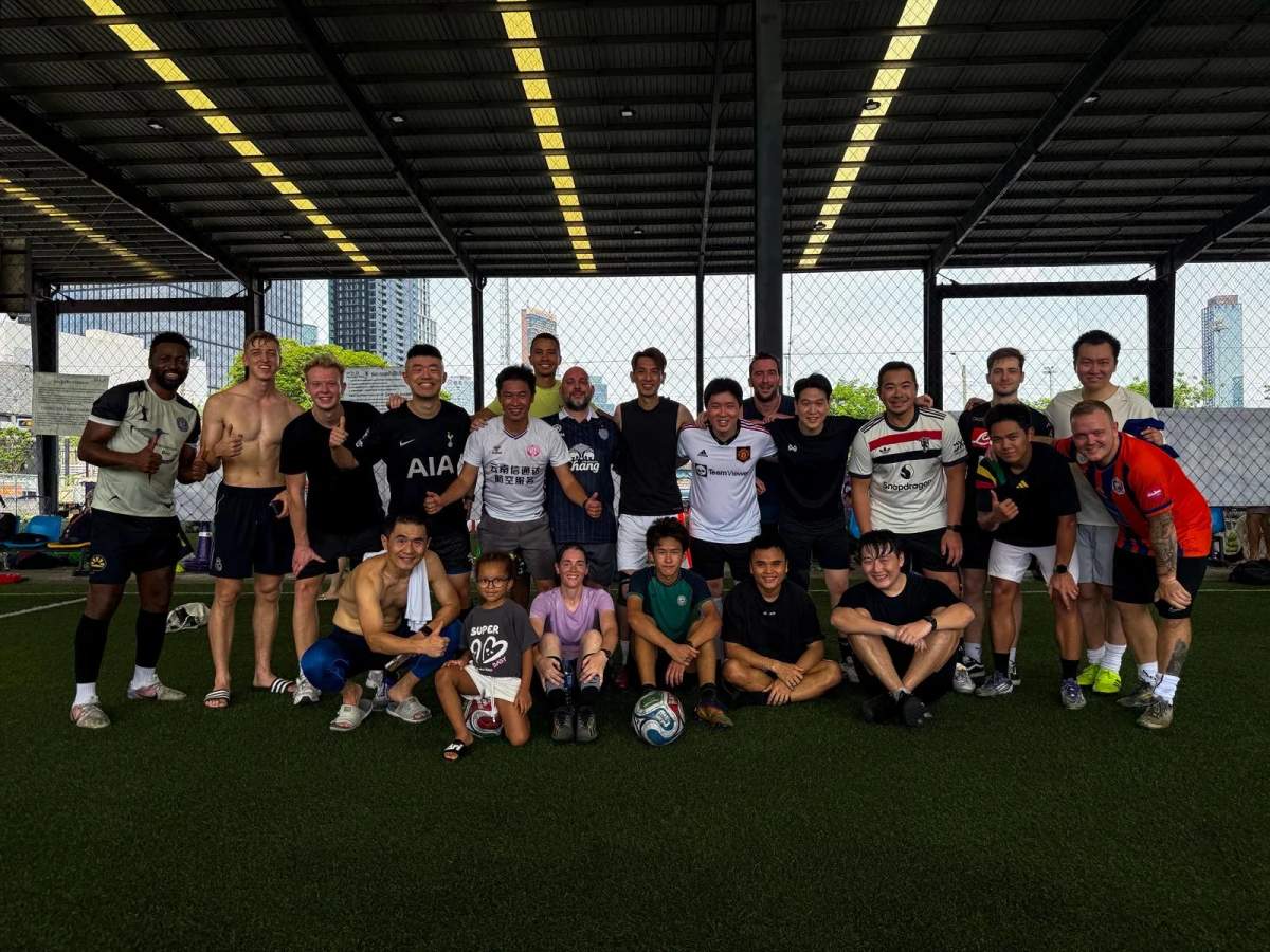 Diverse group of expat football players gathering at POLO Football Park in Bangkok for a pickup football game under floodlights