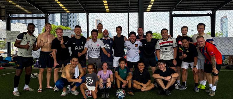 Diverse group of expat football players gathering at POLO Football Park in Bangkok for a pickup football game under floodlights